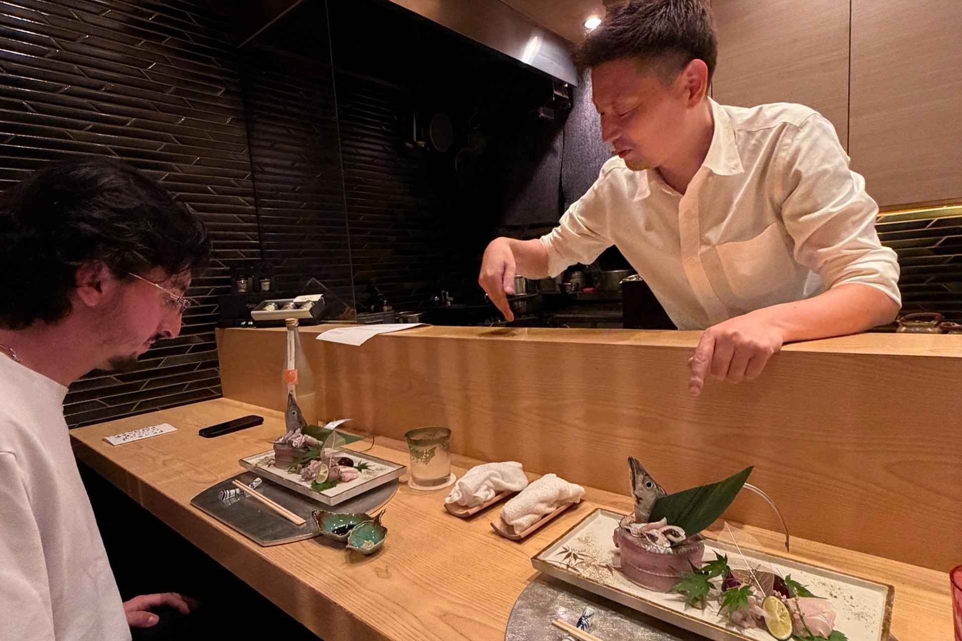 The chef talking across the counter to a guest, with the day’s sashimi plated